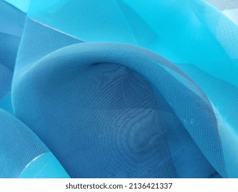 Turquoise blue transparent fabric with a golden thread and with a large rounded fold in the center (macro, texture).