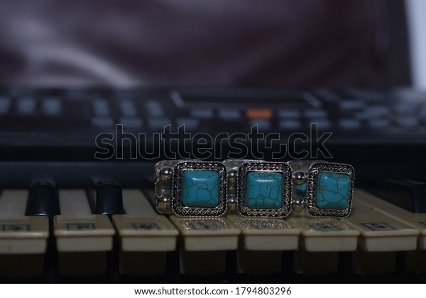 Turquoise\
It\'s a turquoise bracelet. Placed on the\
piano keys