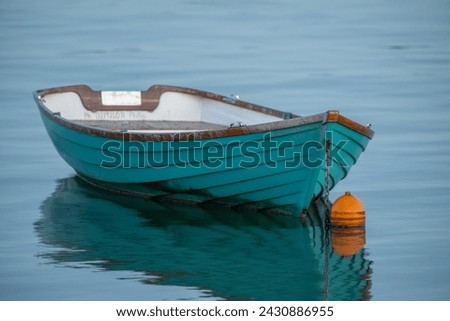 Turquoise dingy with an orange mooring bouy reflected in shallow water