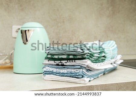 turquoise electric kettle in retro style and a stack of various kitchen towels in a bright kitchen. Kitchen interier