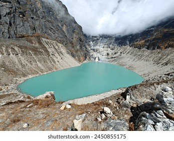 A turquoise glacial lake nestled in the Himalayan mountains of Nepal, with cloudy skies above. 