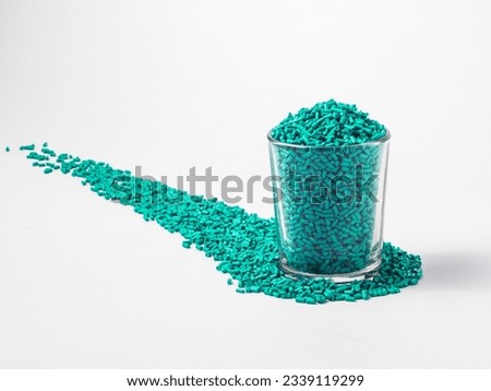 Turquoise masterbatch granules of cold cut type, placed in a glass cup on a white background, this polymers is used as a colorant for products in the plastics industry