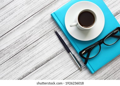 A turquoise notebook, a white coffee cup, glasses, and a ballpoint pen on a wooden background. Close up, top view, diagonal composition. Office picture.