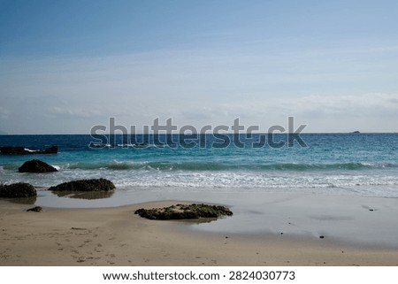 Turquoise ocean waves lapping on sandy beach with green rocks in Shimoda