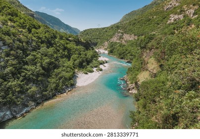 Turquoise river flowing through a deep canyon, surrounded by lush green forested mountains under a clear blue sky creating a serene wilderness landscape
