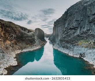 Turquoise river flows through basalt column walls at Studlagil Canyon, Iceland.