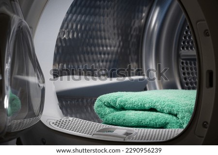 Turquoise towel are stacked in the tumble dryer. Laundry. Clean concept. Washing machine with open door in dark room