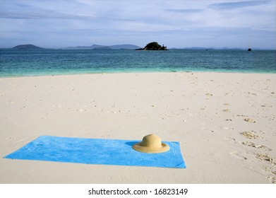 A Turquoise Towel And Sun Hat On A White Beach