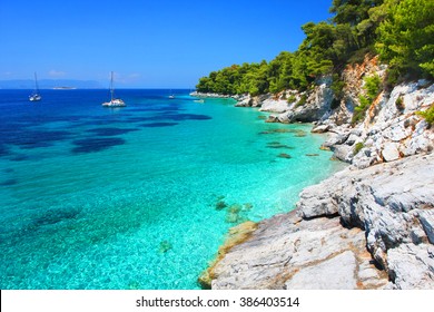 Turquoise waters with cliffs and anchoring sailboats in the neighborhood of Kastani beach (another filming location of Mamma Mia! musical), Skopelos island, Greece 