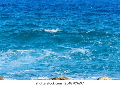 Turquoise waves gently crash against the rocky coastline, sparkling under the summer sun, evoking tranquility. - Powered by Shutterstock