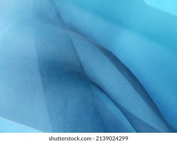 Turquoise-blue transparent fabric with a gold thread and a curved rounded fold in the center (macro, texture).