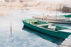 A Turquoise-colored Wooden Boat Anchored In The Bay. Old Rowboats Moored On The Frozen Lake During Winter.