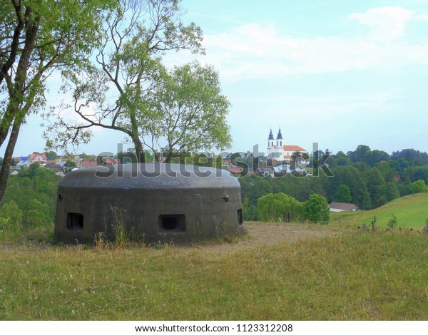 Turret of a bomb\
shelter in the hill with the view of a town and a nearby Catholic\
church with a visible\
horizon