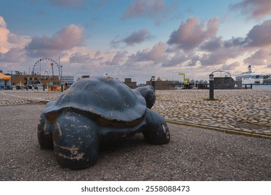 A turtle sculpture stands in a public space in Helsinki, Finland. A ferris wheel and cruise ship are visible in the background, set against an overcast sky. - Powered by Shutterstock