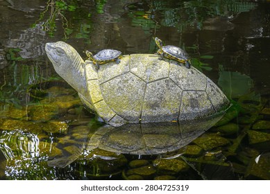 Turtles Resting on a Stone Turtle Sculpture in a Pond