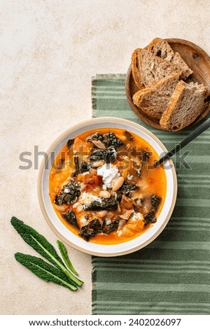 Tuscan kale soup, homemade meal, with veggies, cabbage, carrot, tomato, potato and white beans, fried bacon and sour cream, bread plate. Vertical image.
