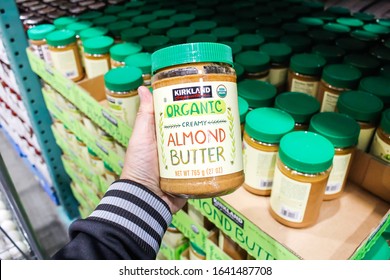 Tustin, California/United States - 02/08/2020: A Hand Holds A Jar Of Kirkland Signature Organic Creamy Almond Butter On Display At A Local Costco.