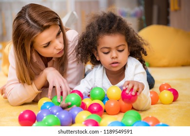 Tutor And Adorable African American Child Playing With Colorful Balls In Kindergarten