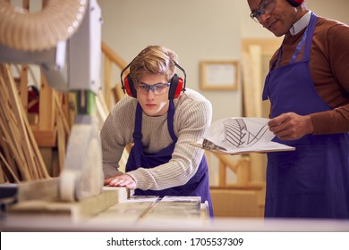 Tutor With Male Carpentry Student In Workshop Studying For Apprenticeship At College Using Bench Saw