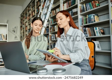 Tutoring session in the library, a redhead tutor and a teenage girl, work on a laptop for modern education.