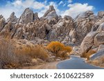 Tuttle Creek Road winds through boulder landscape with fall color under blue sky with puffy clouds, Alabama Hills, Lone Pine, CA