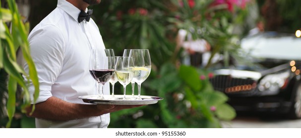 Tuxedo dressed waiter serving wine in a fancy outdoor setting.