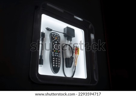 TV accessories: infrared remote controls, component video cables, power adapters in showcase with illumination in dark room at exhibition, trade show. Electronic, entertainment, equipment concept