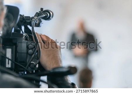 TV camera recording official statement at press conference. Captures structured communication, clarity, and professional media documentation.