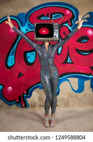 Tv head woman infront of the word love graffiti painted on a wall