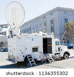 TV production van with satellite dish parked near urban government building.