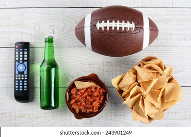 TV Remote, Beer Bottle, Bowl Of Chips With Salsa And An American Style Football On A Rustic Whitewashed Wood Surface. Horizontal Format. Great For Super Bowl Party Themed Projects.