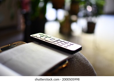 TV remote control isolated on the arm of a couch. Black remote control sits alone with a bokeh background. Small remote control. Sound Bar remote control.