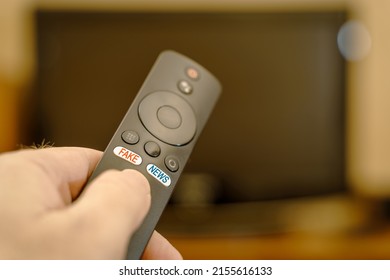 TV remote in hand with inscriptions on the buttons fake and news. The inscription fake in red and the inscription news in blue on the buttons of the TV remote control.