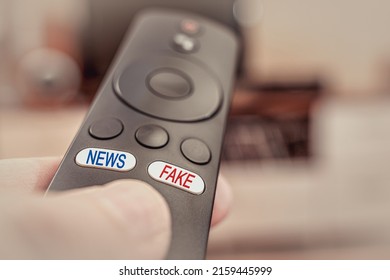 TV remote in hand with inscriptions on the buttons fake and news. The inscription fake in red and the inscription news in blue on the buttons of the TV remote control.