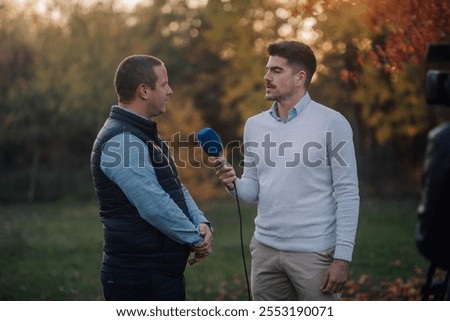Tv reporter interviews a farmer at sunset in a field, discussing agriculture passionately. The warm light creates a serene atmosphere