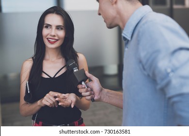 TV Reporter At Work. A Beautiful Girl Smiles Thoughtfully. A Journalist In The Street Holds A Microphone Next To Her And Is Waiting For A Reply