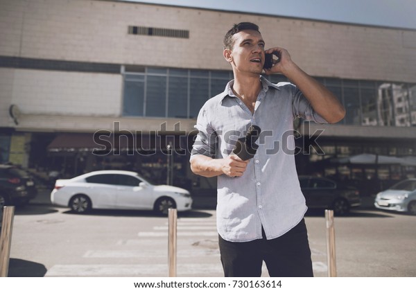 TV reporter at work. On the street the\
correspondent looks up while talking on the phone. Behind him is a\
white car and a building with\
windows