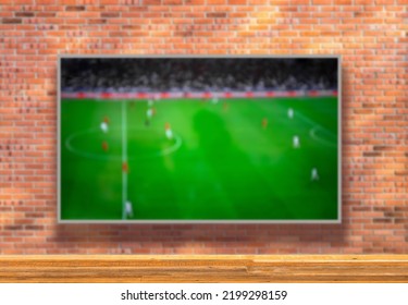 TV with soccer field on brick wall and wooden table with empty space. Selective focus. Blurred background.
