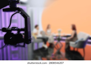 TV Studio camera rig framing panelists on colored talk set.
