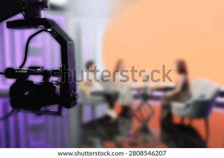 TV Studio camera rig framing panelists on colored talk set.