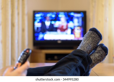 TV, Television Watching (news) With Feet On The Table And Remote In Hand - Stock Photo