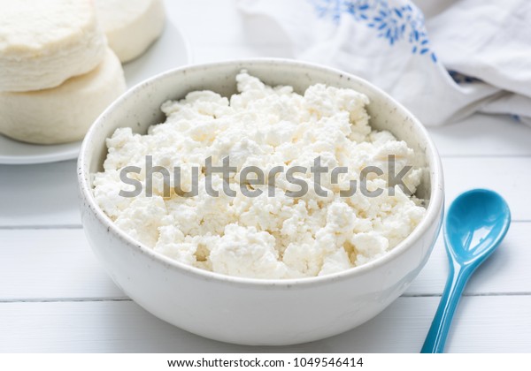 Tvorog, farmers cheese, curd cheese or cottage\
cheese in white bowl on white wooden table, closeup view. Rich in\
calcium healthy food