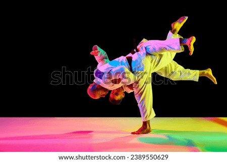 Tw fit man in uniform, professional sportsmen of martial arts, fighting, training before fight in neon isolated black background. Concept of combat sport, health, strength, energy, fit. Copy space