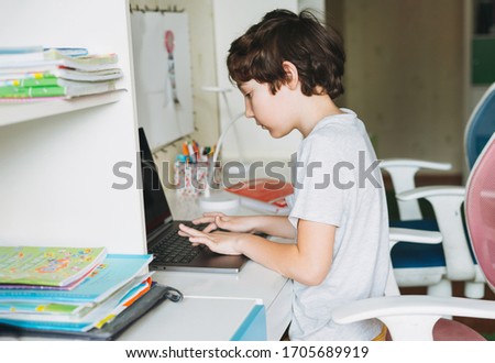 Tween boy do homework learn foreign language writing in pupil book with opened laptop at the room home dictance education