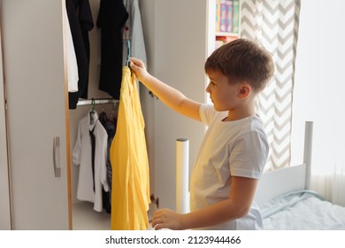 Tween Boy Getting Ready For School In The Morning. Cute Little Boy Open The Closet Wardrobe With Clothes And Making Choise What To Wear.