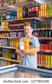 Tween Boy Standing Among Shelves In Supermarket, Satisfied With Sweet Drinks