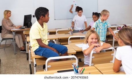 Tween Boys And Girls Friendly Talking In Break Between Lessons Sitting In Classroom