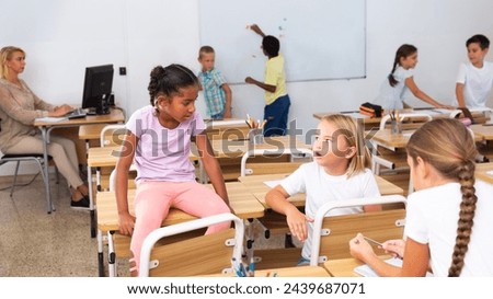 Tween boys and girls friendly talking in break between lessons sitting in classroom