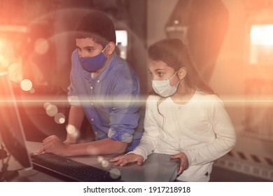 Tween girl and boy in protective masks using computer while trying to find solution of conundrum in quest room. New norms in pandemic, precaution for viral infections. Toned image