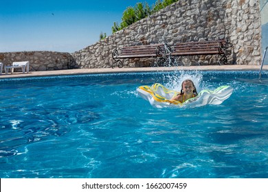 Tween Girl Playing, Splashing, Laughing And Have Fun In The Blue Water Of Swimming Pool With Inflatanle Rings.